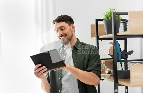 Image of happy smiling man with tablet pc at shelf at home