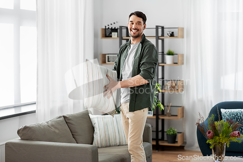 Image of happy smiling man arranging sofa cushions at home