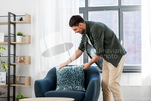 Image of happy smiling man arranging chair cushion at home