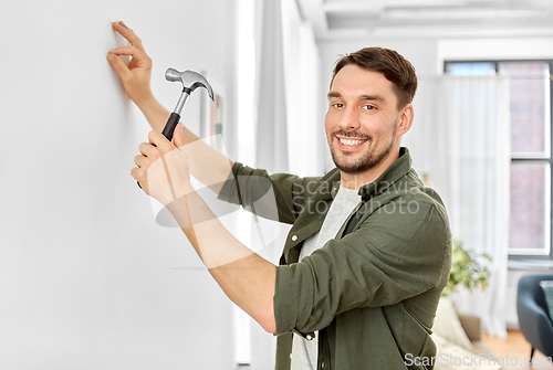 Image of smiling man hammering nail to wall at home