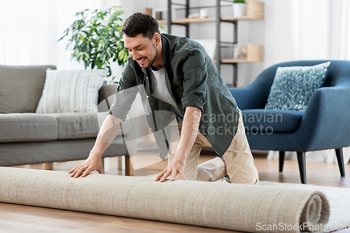 Image of happy smiling young man unfolding carpet at home