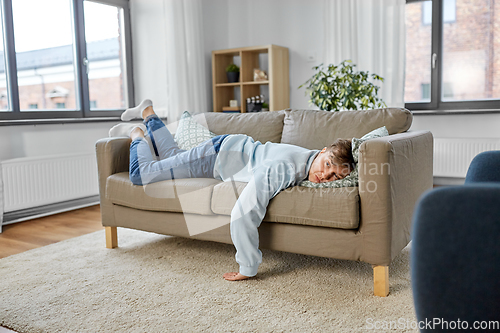 Image of bored or lazy young man lying on sofa at home