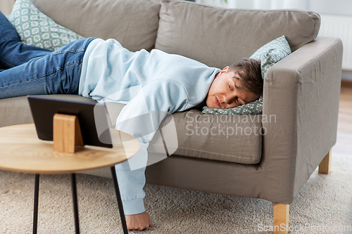 Image of bored man with tablet pc lying on sofa at home