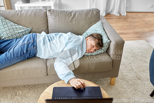 Image of bored man with laptop lying on sofa at home