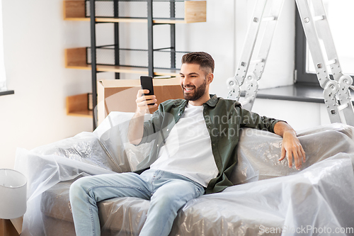 Image of man with smartphone and boxes moving into new home