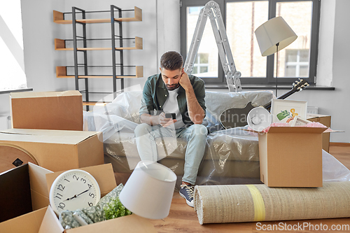 Image of sad man with smartphone and boxes moving home