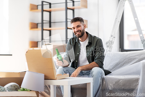 Image of man with box of pizza and beer bottle at new home