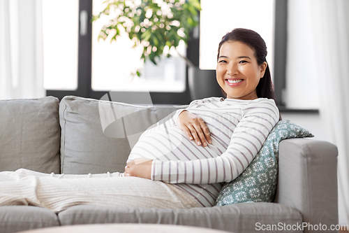 Image of happy pregnant asian woman sitting on sofa at home