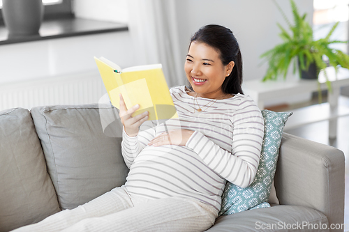 Image of happy pregnant woman reading book at home