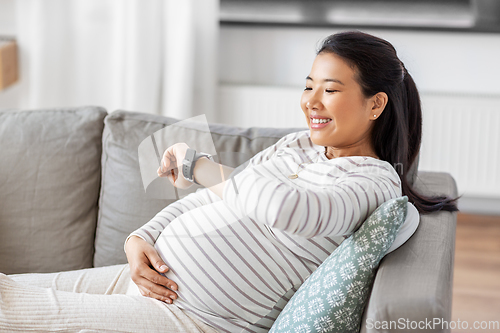 Image of happy pregnant woman with smart watch at home