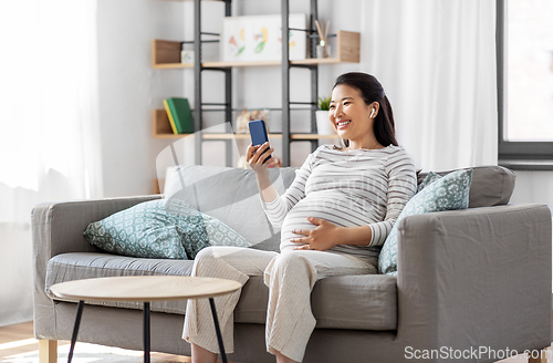 Image of pregnant woman with phone and earphones at home