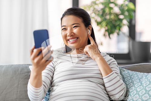 Image of pregnant woman with phone and earphones at home