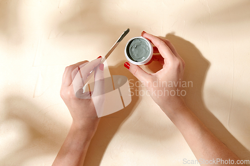 Image of hands holding jar of blue cosmetic clay mask