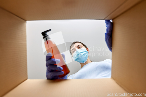 Image of woman in mask unpacking parcel box with cosmetics