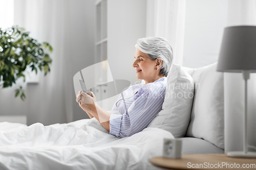 Image of happy senior woman using smartphone in bed at home