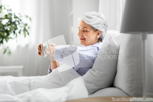 Image of happy old woman with health tracker sitting in bed