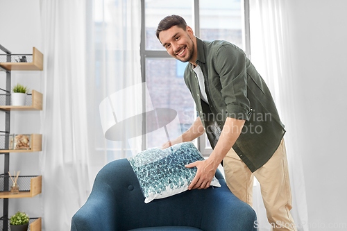 Image of happy smiling man arranging chair cushion at home