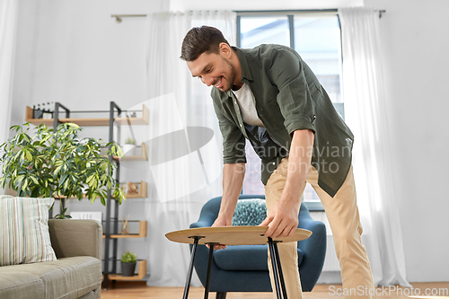 Image of man placing coffee table next to sofa at home