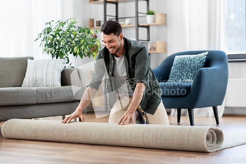 Image of happy smiling young man unfolding carpet at home