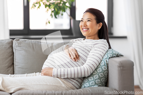 Image of happy pregnant asian woman sitting on sofa at home