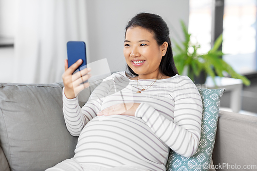 Image of happy pregnant woman with smartphone at home