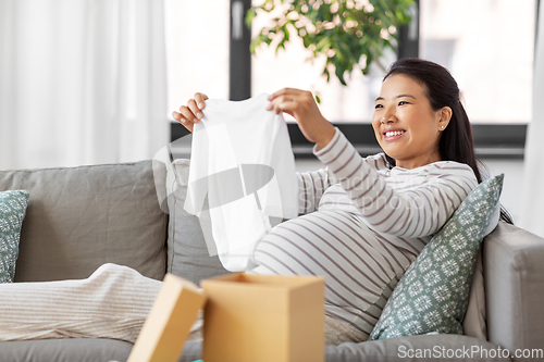 Image of happy pregnant woman with baby's bodysuit at home