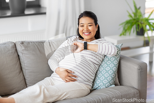 Image of happy pregnant woman with smart watch at home