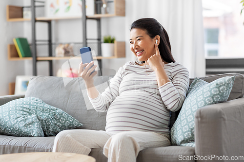 Image of pregnant woman with phone and earphones at home