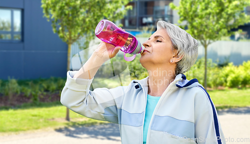 Image of old woman drinking water after exercising in city