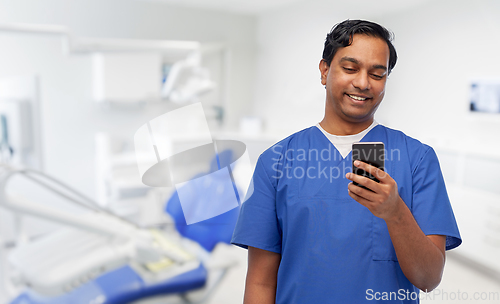 Image of smiling doctor using smartphone at dental office