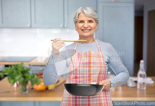 Image of smiling senior woman in apron with frying pan