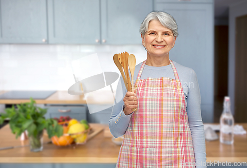 Image of smiling senior woman in apron with wooden spoons