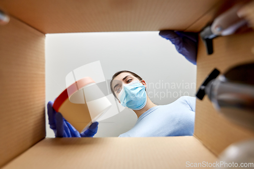 Image of woman in mask unpacking parcel box with cosmetics