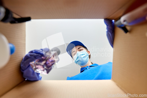 Image of woman in mask packing parcel box with cosmetics