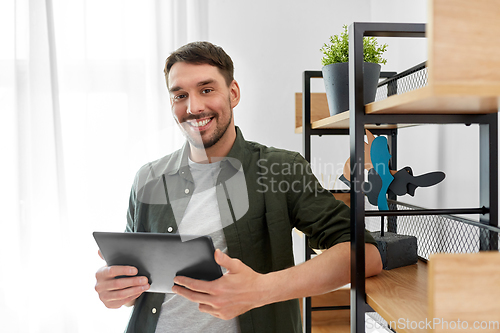 Image of happy smiling man with tablet pc at shelf at home