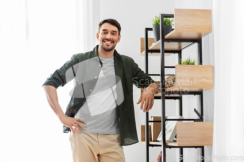 Image of happy smiling man standing at shelf at home