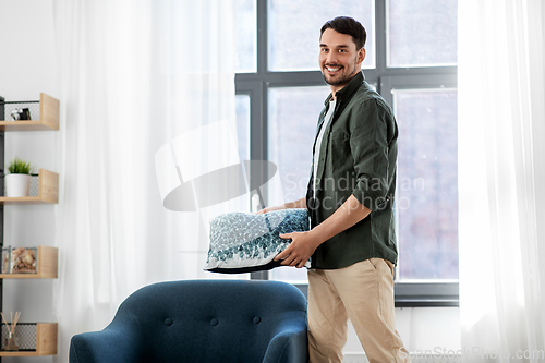 Image of happy smiling man arranging chair cushion at home