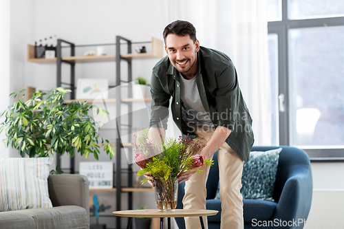 Image of man placing flowers on coffee table at home