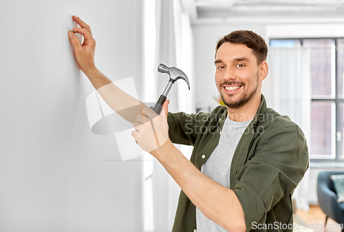 Image of smiling man hammering nail to wall at home