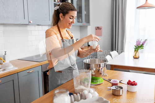 Image of happy young woman cooking food on kitchen at home