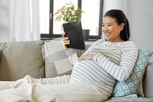 Image of happy pregnant asian woman with tablet pc at home