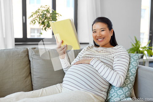 Image of happy pregnant woman reading book at home