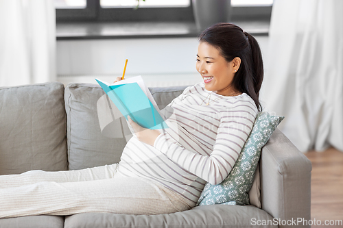 Image of happy pregnant woman writing to diary at home