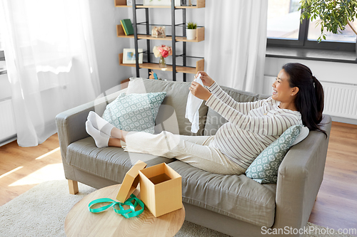 Image of happy pregnant woman with baby's bodysuit at home