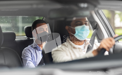 Image of male driver in mask driving car with passenger