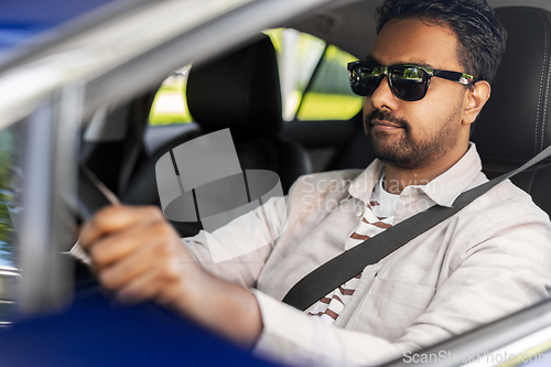 Image of smiling indian man in sunglasses driving car