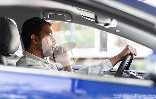 Image of indian man driving car and calling on smartphone