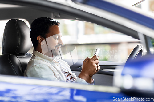 Image of smiling indian man in car using smartphone