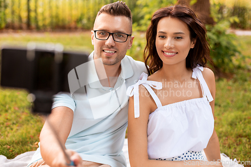 Image of happy couple taking selfie at picnic in park
