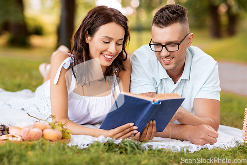 Image of happy couple reading book on picnic at summer park